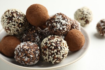 Tasty chocolate candies with cocoa powder, nuts and sesame seeds on white table, closeup
