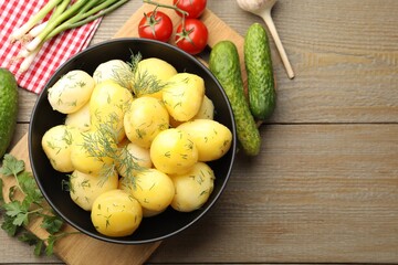 Tasty young boiled potatoes with dill in bowl and products on wooden table, flat lay. Space for text