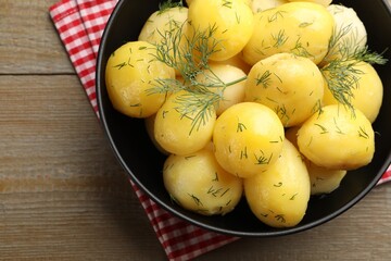Tasty young boiled potatoes with dill and oil in bowl on wooden table, top view