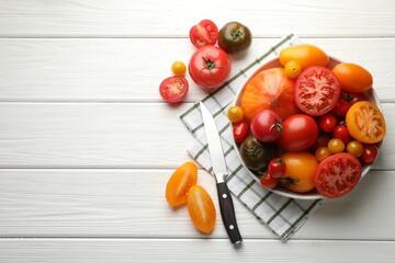 Different ripe tomatoes and knife on white wooden table, flat lay. Space for text