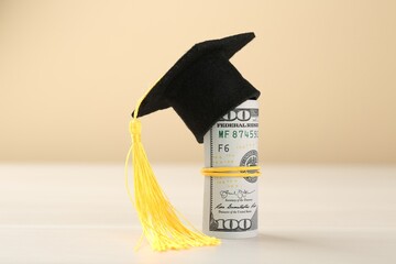 Scholarship. Graduate hat and dollar banknotes on white table against beige background, closeup