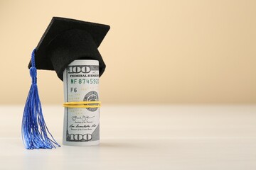 Scholarship. Graduate hat and dollar banknotes on white table against beige background, closeup....