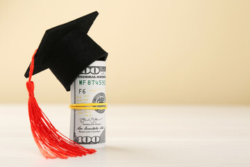Scholarship. Graduate hat and dollar banknotes on white table against beige background, closeup....