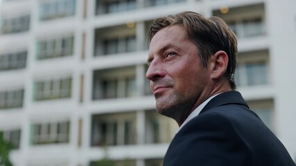 Portrait of satisfied businessman looking aside against modern buildings in downtown block. Experienced entrepreneur in suit radiates success while stands on city street closeup