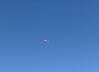 Airplane flying in clear blue sky at high altitude with visible red tailfin. Aviation, transportation, speed, and global connectivity through air travel.