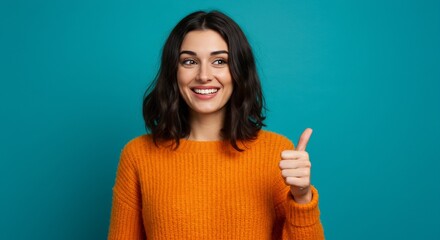 Cheerful Young Woman in Orange Sweater Giving Thumbs Up with a Bright Smile Against a Teal Background, Positive Gesture