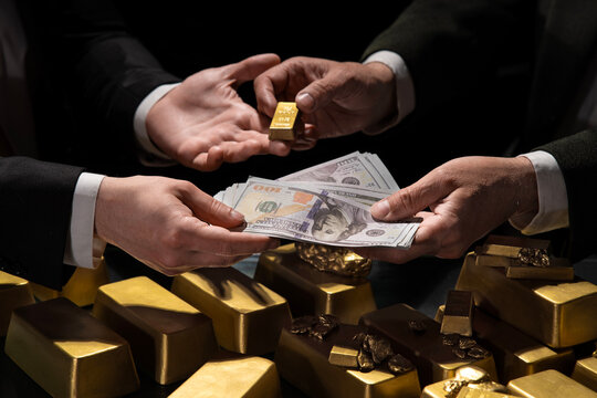 A hand giving a gold bar to another person holding a wad of dollar bills. Gold Nuggets. Bank gold bars. Gold reserv holdings concept. Savings and investments, business and finance