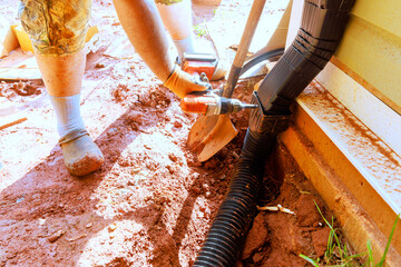 Person uses drill to connect parts of drainage system in garden area.