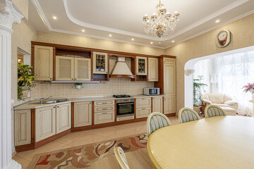 Elegant kitchen featuring wooden cabinets, a chandelier, and a round dining table. Adjacent living room with a sofa is visible through an archway