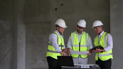 Three construction engineers collaborating on-site using a laptop and tablet while discussing project plans in an unfinished building. Ideal for smart construction and teamwork concepts.
