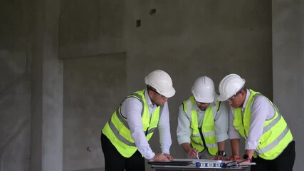 Three construction engineers collaborating on-site using a laptop and tablet while discussing project plans in an unfinished building. Ideal for smart construction and teamwork concepts.
