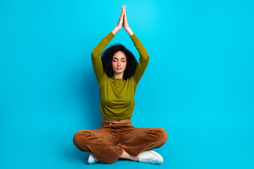 Serene young woman meditating in casual attire against a vibrant blue backdrop, practicing...