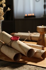 Old paper scrolls and burning candle on wooden table, closeup
