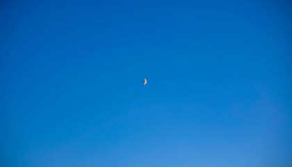 Pale crescent moon in a vast blue sky