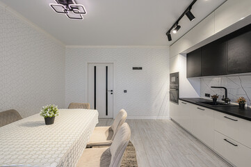 modern kitchen with white and black cabinets, a dining table with tan chairs, patterned wallpaper, and stylish lighting