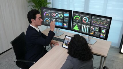 Team of business analysts analyzing financial dashboard charts on dual monitors. Professional colleagues discussing data strategy using digital tablet in modern corporate office. - Powered by Adobe