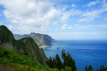 Scenic view of Penha de Águia rock formation in Porto da Cruz, Madeira, Portugal, with dramatic green cliffs and the Atlantic Ocean under a bright blue sky.