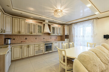 classic kitchen and dining area features cream and gold cabinetry, a chandelier, tiled backsplash,...