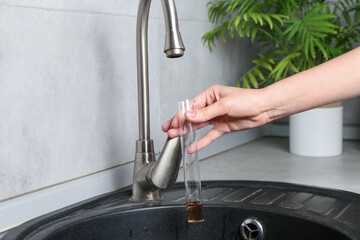 Woman taking sample of water from faucet indoors, closeup. Quality testing