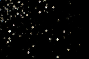 Abstract defocused light spots on black background featuring circular bokeh patterns.