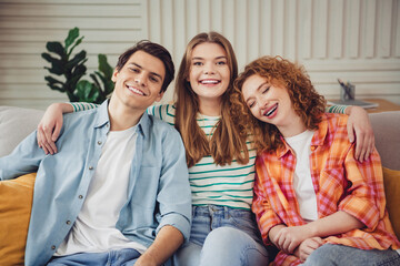 Three cheerful friends relaxing at home on a couch, enjoying each other's company and laughing...