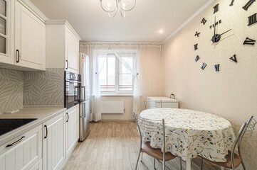 bright kitchen features white cabinetry, stainless steel appliances, a round table with floral tablecloth, a large wall clock, and light wood flooring