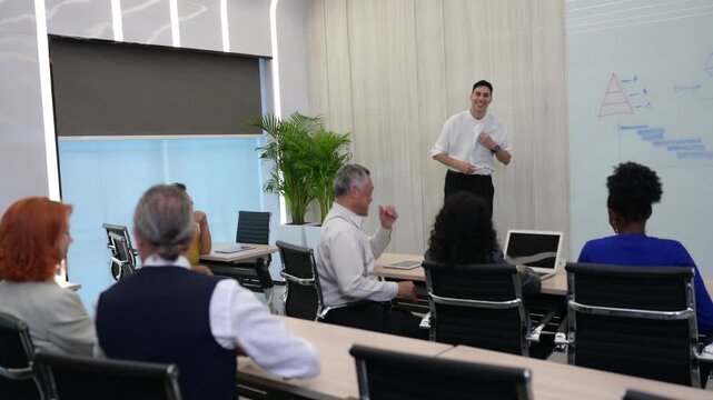 Confident male speaker giving business presentation to diverse corporate team in modern conference room. Professional coach leading workshop seminar near whiteboard with diagrams. - Powered by Adobe