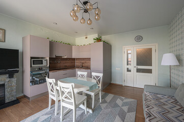 cozy kitchen and living area with a round table, white chairs, and a modern chandelier. The kitchen features gray cabinets and wooden accents, creating a warm ambiance