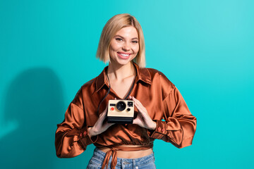 Smiling young woman holding a vintage camera against a teal background showcasing trendy style and...