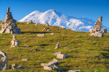 panoramic view of the Bolshoy Bermamyt plateau with stone turrets built on a grassy slope, with the snow-capped peaks of Mount Elbrus in the background, at early morning, Stavropol Krai, Russia © Sergey Bogomyako