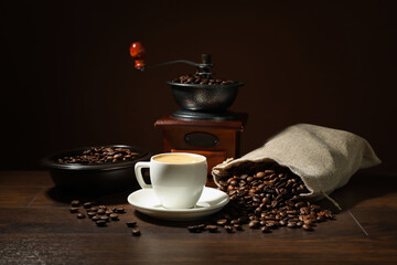 Aromatic coffee in cup, beans and grinder on wooden table against brown background