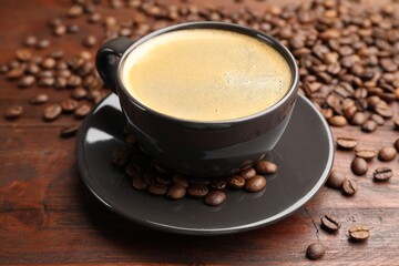 Aromatic coffee in cup and beans on wooden table, closeup