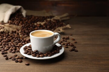Aromatic coffee in cup and beans on wooden table, space for text