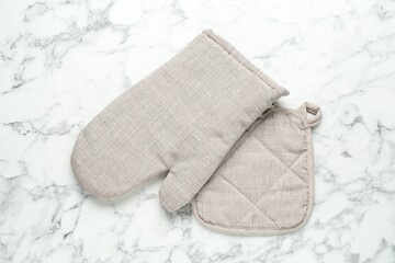 Oven glove and potholder on white marble table, flat lay
