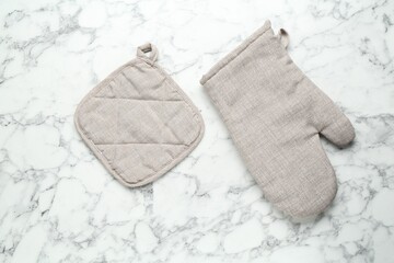Oven glove and potholder on white marble table, flat lay