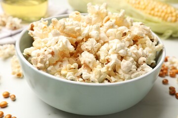 Tasty popcorn and corn kernels on white marble table, closeup