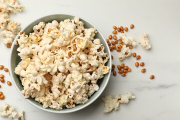 Tasty popcorn and corn kernels on white marble table, flat lay