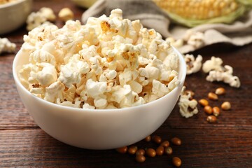 Tasty popcorn and corn kernels on wooden table, closeup