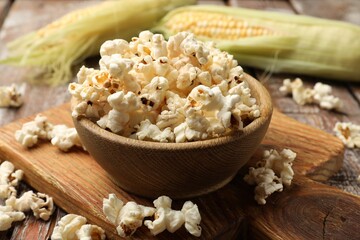 Tasty popcorn and corncobs on wooden table, closeup