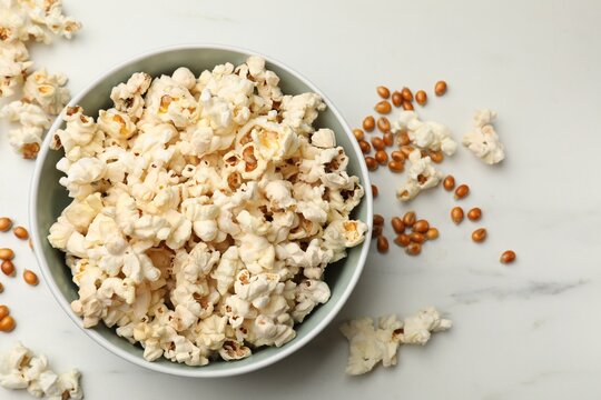 Tasty popcorn and corn kernels on white marble table, flat lay