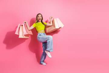 Cheerful young woman carrying shopping bags with a vibrant smile on a pink background showcasing...