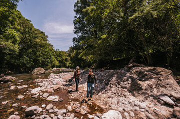 Mother and daughter walking along the riverbank, observing the small details like plants and...