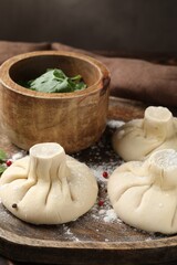Uncooked khinkalis (dumplings) with peppercorns and parsley on table, closeup