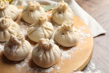 Uncooked khinkalis (dumplings) with flour on wooden table, closeup
