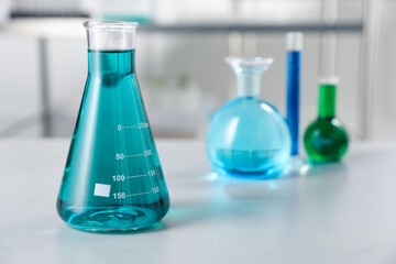Different laboratory glassware with color liquids on light table indoors, selective focus