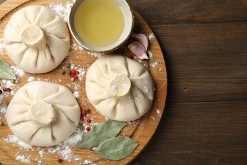 Uncooked khinkalis (dumplings) with peppercorns, flour and bay leaves on wooden table, top view. Space for text