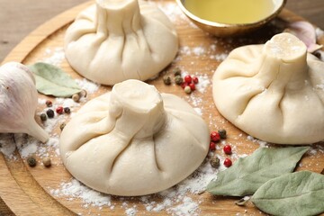 Uncooked khinkalis (dumplings) with peppercorns, flour and bay leaves on wooden table, closeup