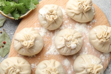 Uncooked khinkalis (dumplings) with peppercorns, flour, parsley and bay leaves on grey table, flat lay