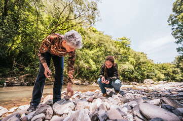 Mother and daughter observing small details like plants, stones, insects, and having a good time by...