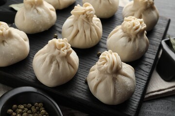 Fototapeta premium Uncooked khinkalis (dumplings) with peppercorns on black table, closeup